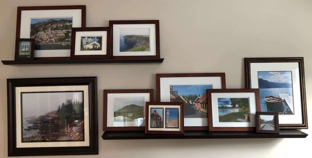 A picture of framed pictures from vacations displayed on wall shelves.