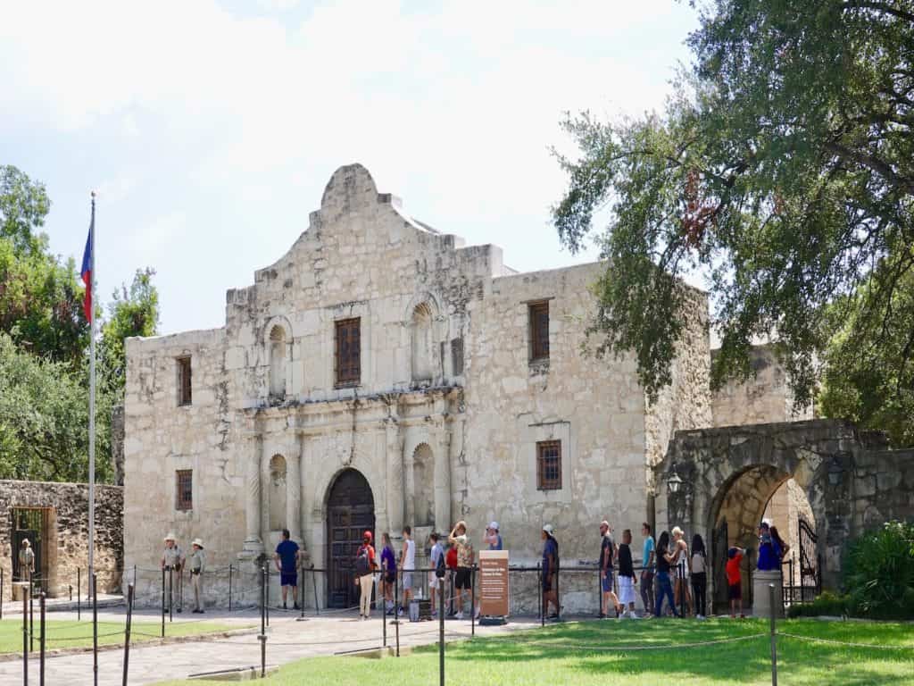 Visitors are lined up to enter a stone mission building