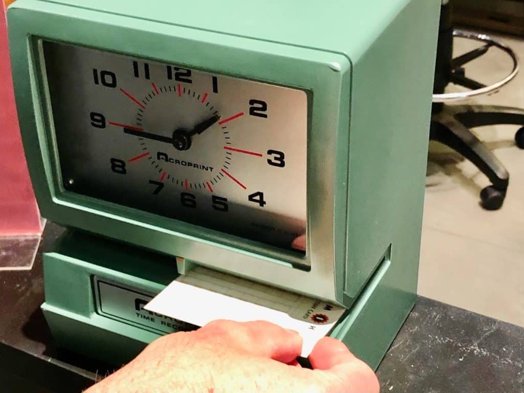 Someone is sticking a time sheet into a vintage time clock.
