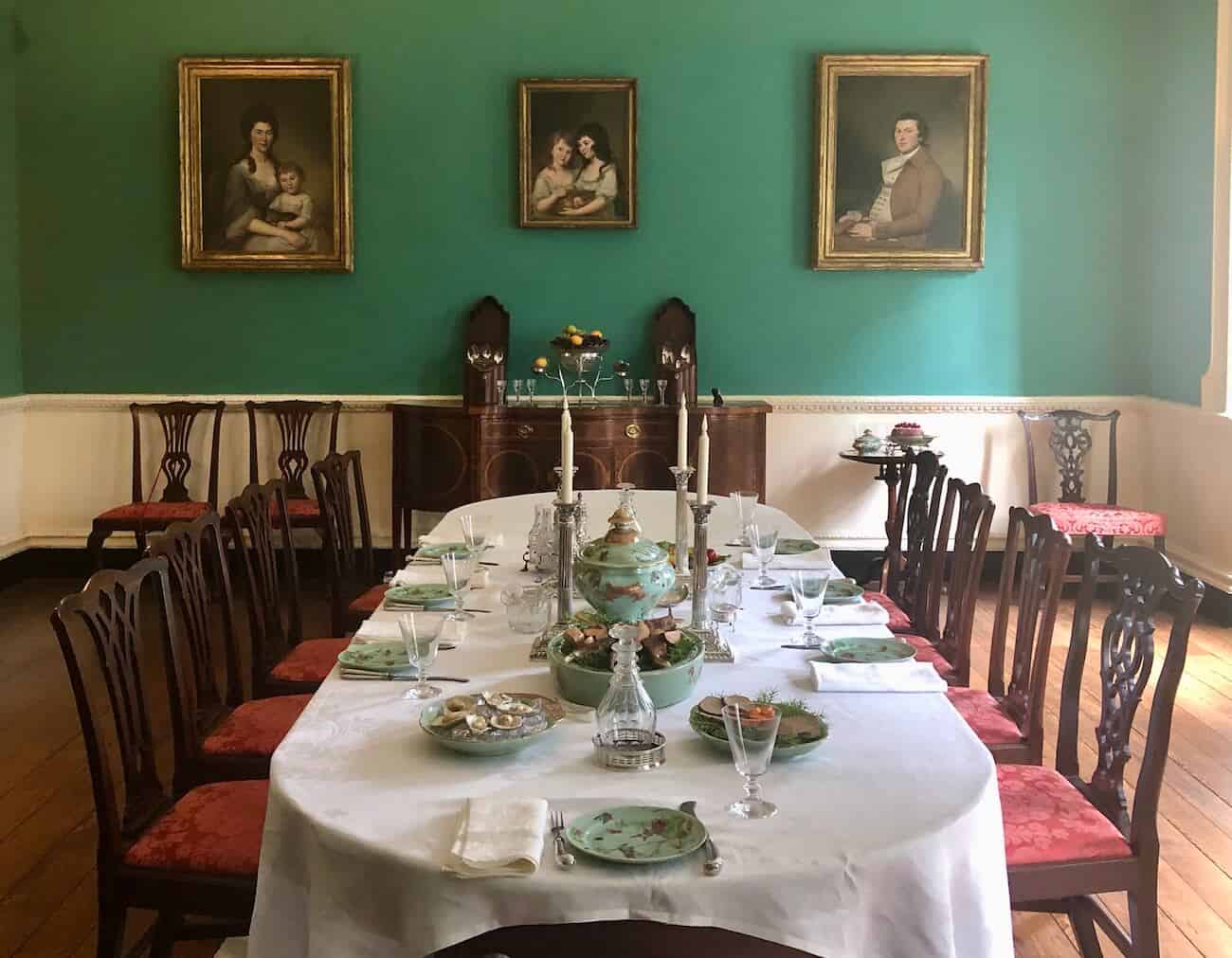 A dining table is set and portraits hang on the walls of a dining room in the Hammond-Harwood House.