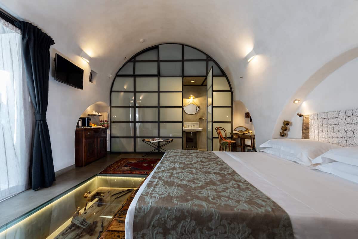 A king-size bed is made up in front of a glassed bathroom in a guest room.