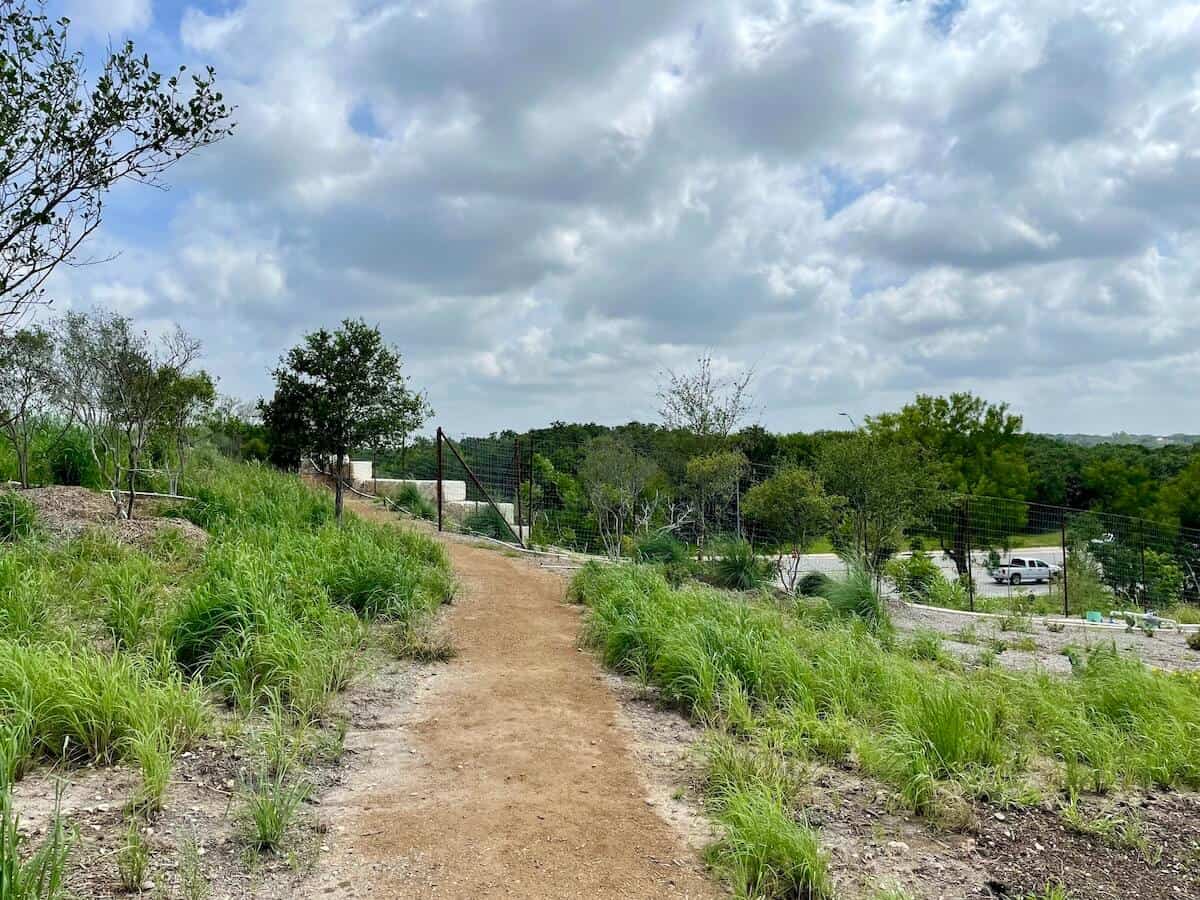 A dirt trail leads through vegetation over a highway at Hardberger Park.