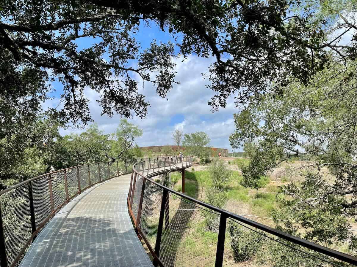 A view of an elevated skywalk that takes walkers above a park to the level of treetops.