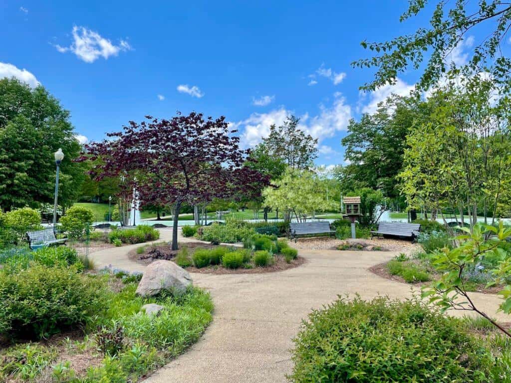 Plants, paths, benches, and a little lending library are in a park.