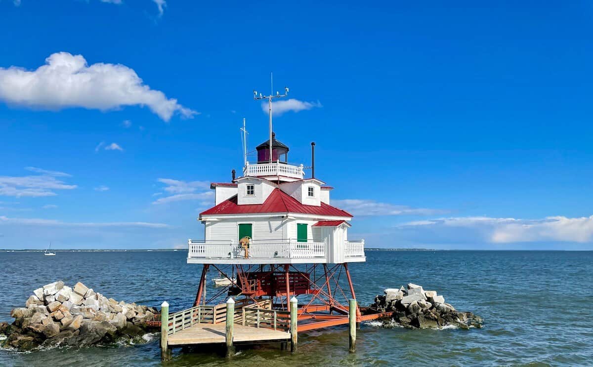 A white lighthouse sits along some rocks in the Chesapeake Bay.
