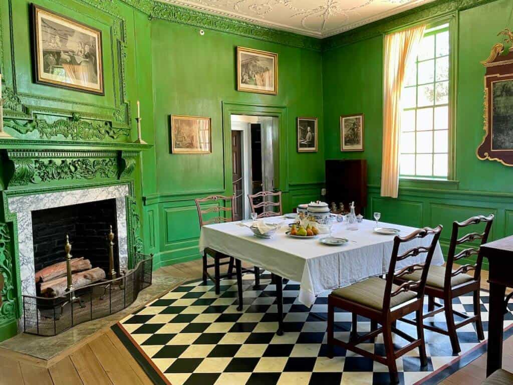 A dining table is set in a room with vivid green walls and a fireplace.