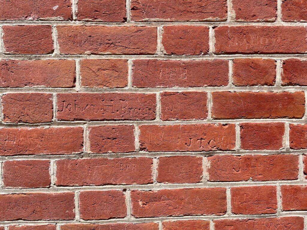 Names are carved into brick on the side of a building.
