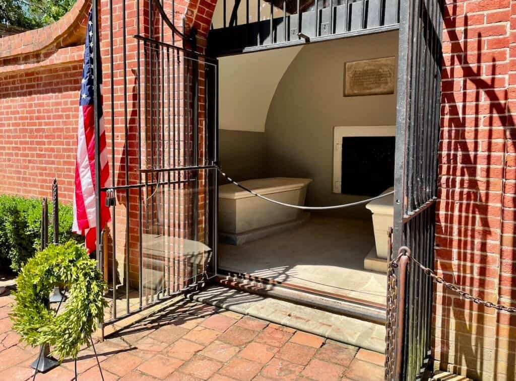 A view of stone coffins inside a tomb; an American flag and a wreath are positioned outside.