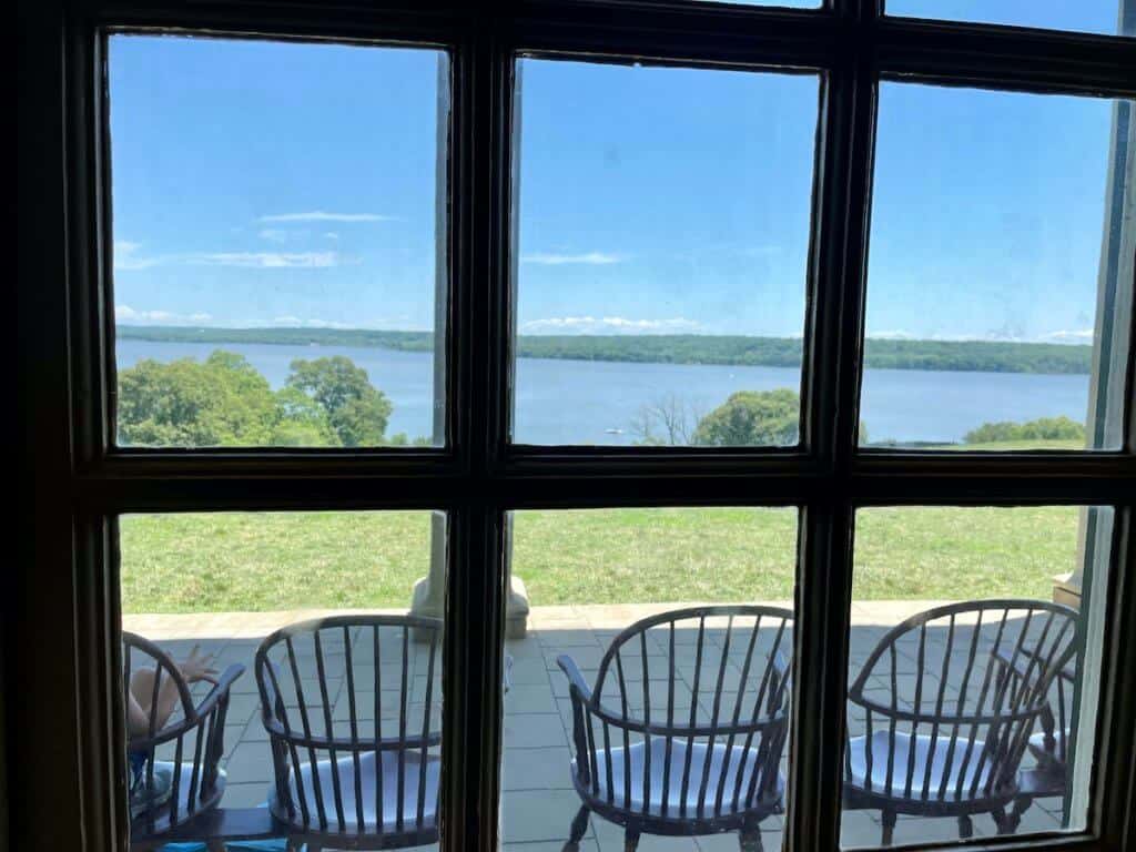 Windsor back chairs sit along a stone patio overlooking a river.