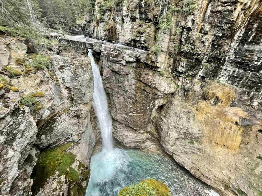 Water spills over rocks into a pool of turquoise water below at Johnston Falls near Banff, CA.