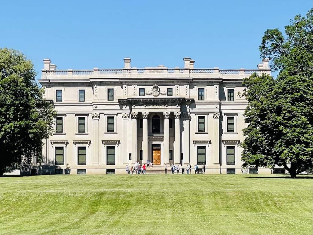 A large stone mansion stans behind an expansive grassy lawn.