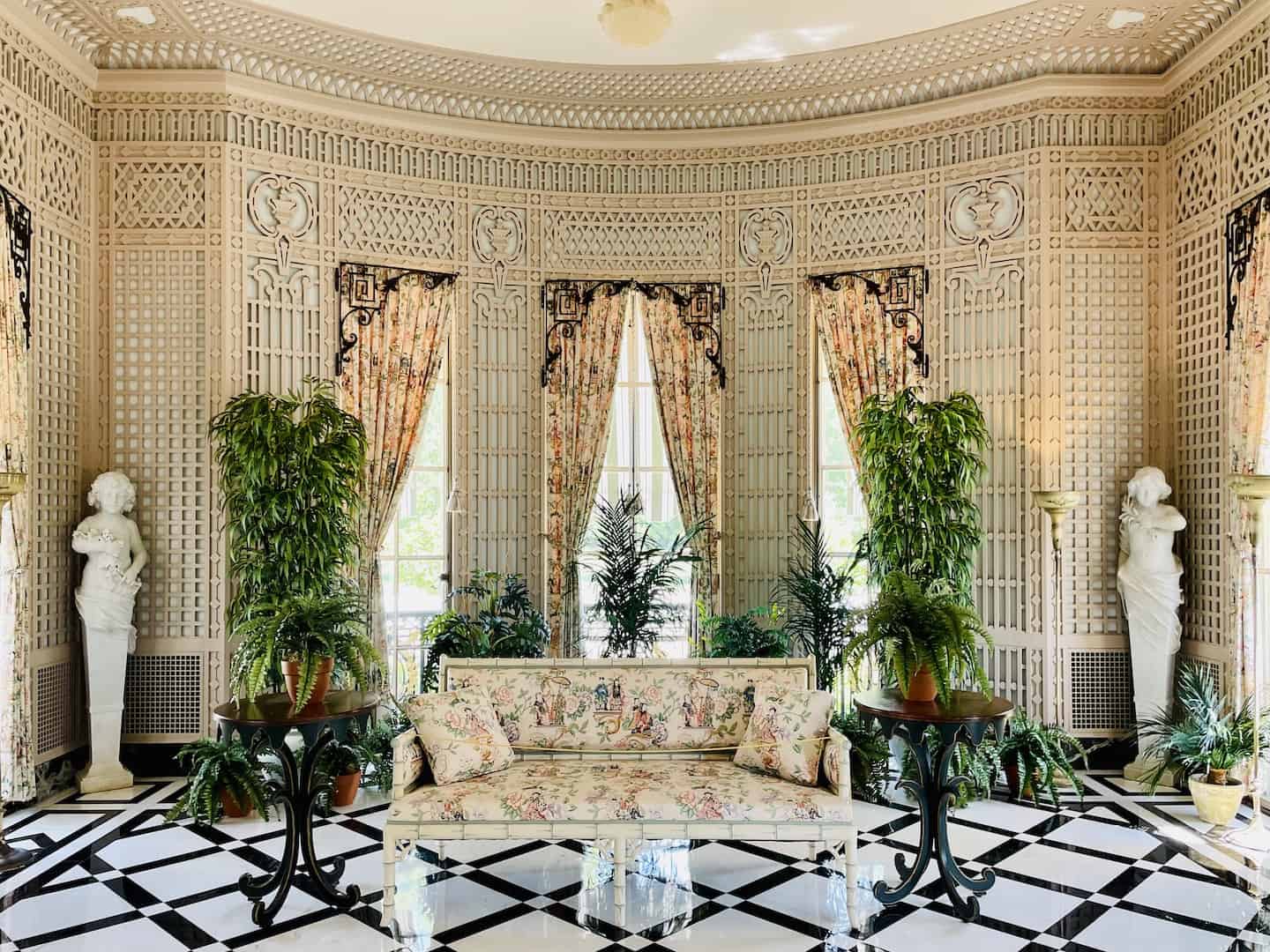 Potted plants, two statues and an upholstered sofa sit on a black and white tiled floor at Nemours Estate.