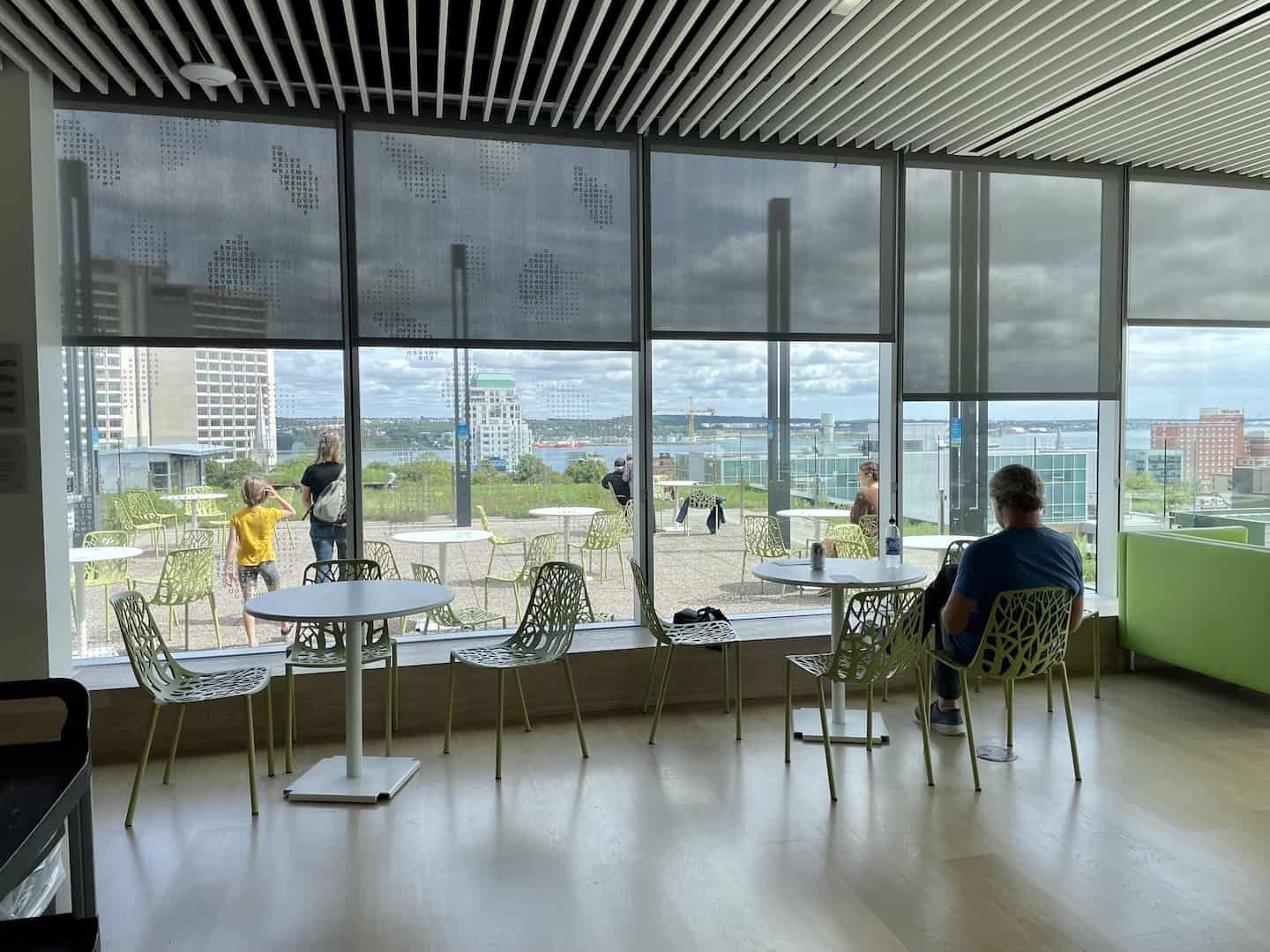 A man sits at a table in a cafe while others walk out on the rooftop deck at the Halifax Public Library.