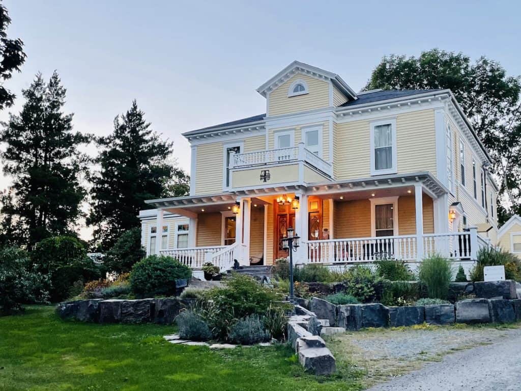 A luxury B&B, Tattingstone Inn is a yellow-sided building with a large wraparound porch in Wolfville, Nova Scotia.