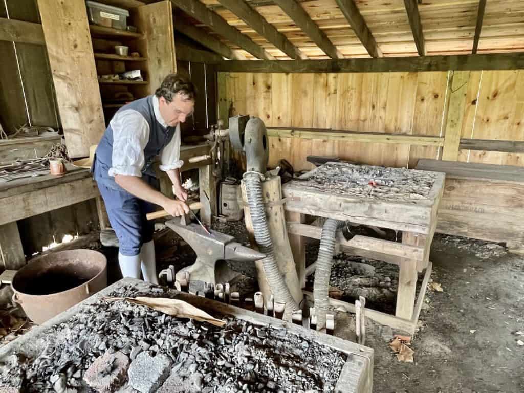 A costumed historical interpreter demonstrates blacksmithing techniques at Colonial PA Plantation near Philadelphia.