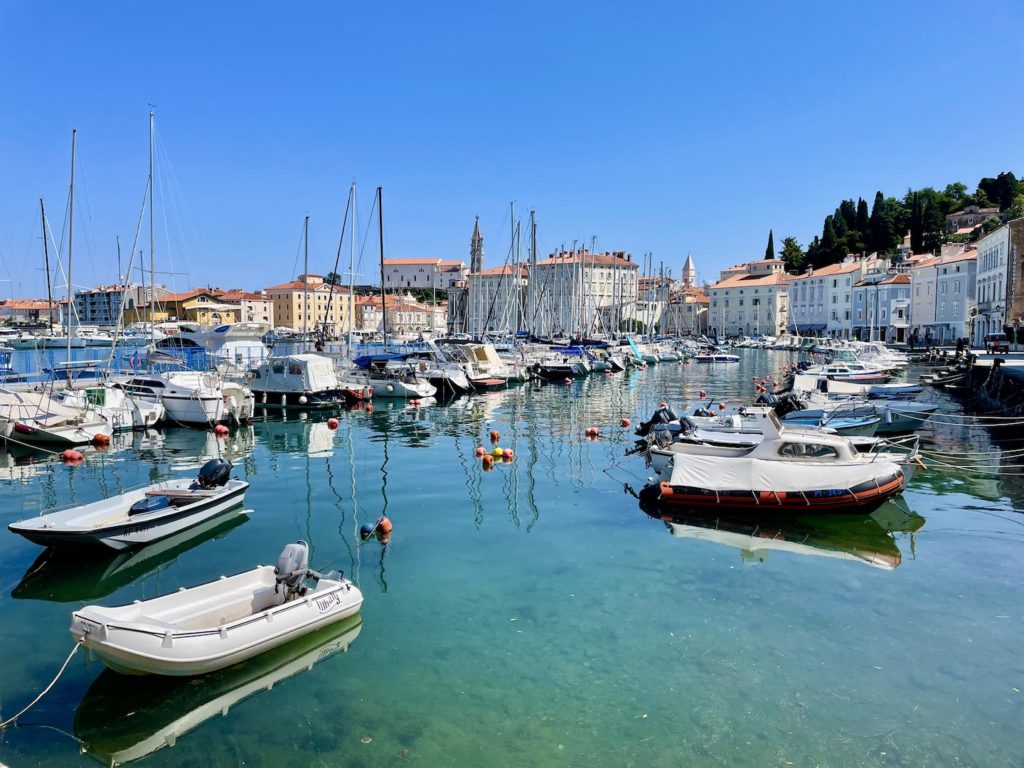 Sailboats and motorboats are docked in a marina and buildings can be seen in the backgorund in Piran, Slovenia.