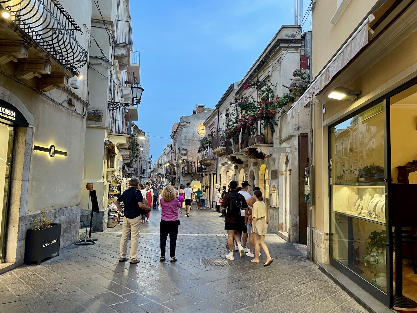 Visitors stroll through a street in Taormina at dusk.