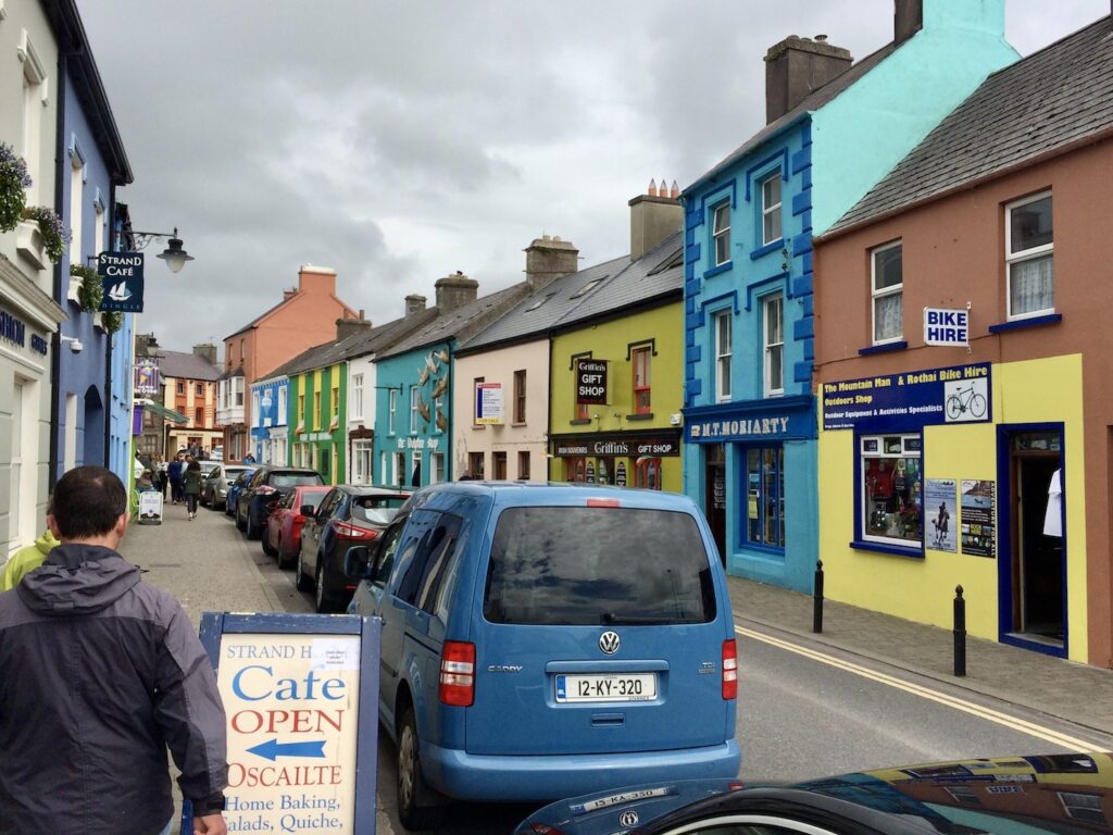 Cars line the road flanked by colorful buildings in Dingle, Ireland.
