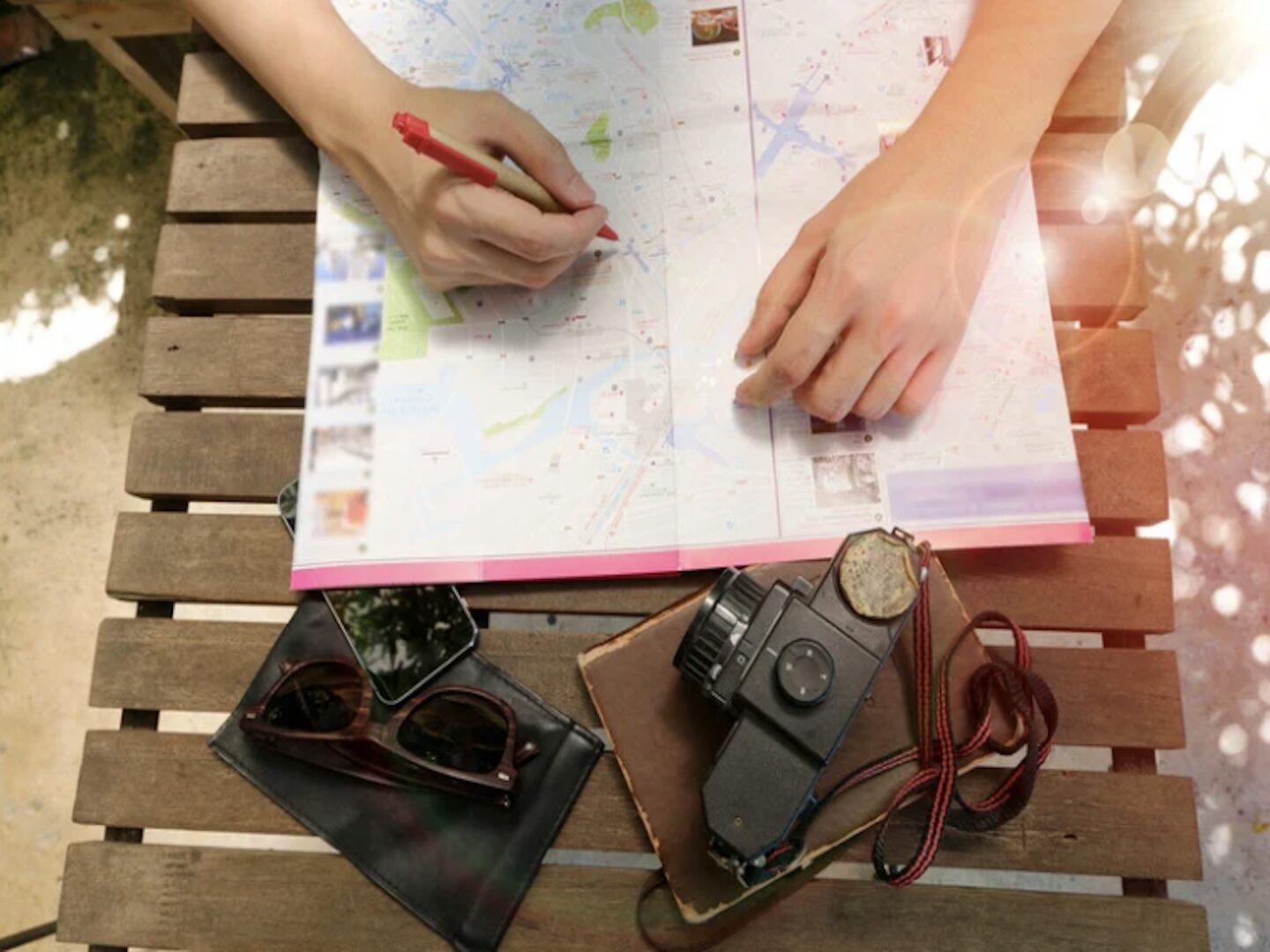 Someone uses a map to plan a trip while sunglasses and a camera rest on the table top.